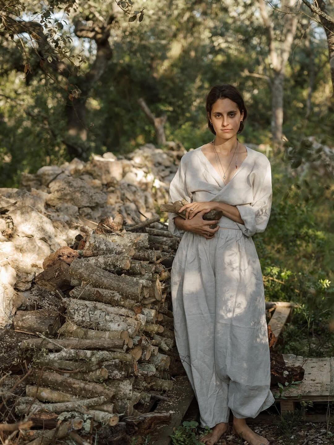 ema in linen in the golden forest, holding gathered wood against her